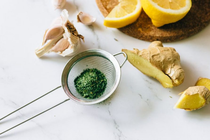A flat lay of garlic, ginger, and lemon on a marble surface for natural remedies.